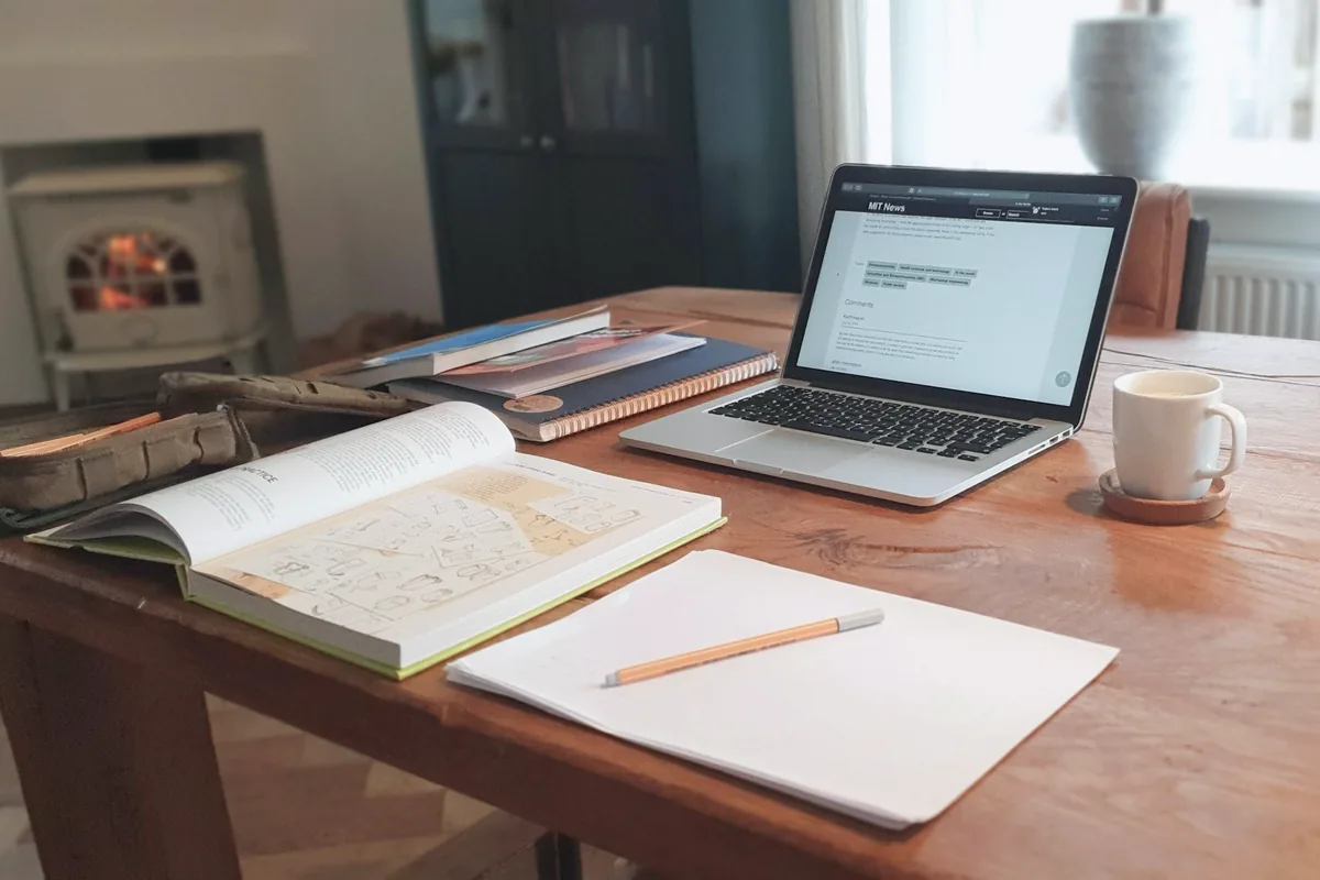 Un bureau en bois avec un ordinateur portable ouvert, un livre ouvert, un cahier et une tasse