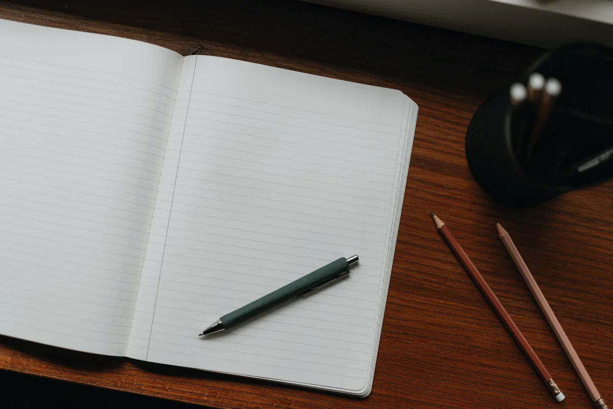 Un carnet ouvert aux pages vierges posé sur un bureau en bois, avec un stylo et des crayons