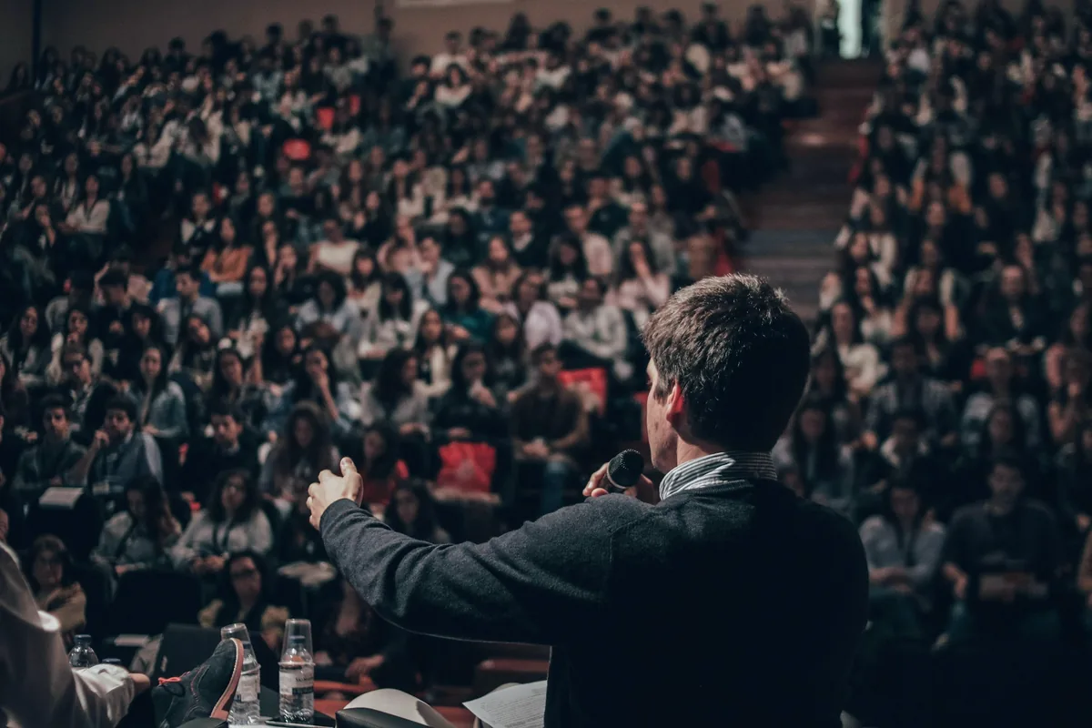 Un orateur vu de dos s’adresse à une grande salle pleine, dans un amphithéâtre