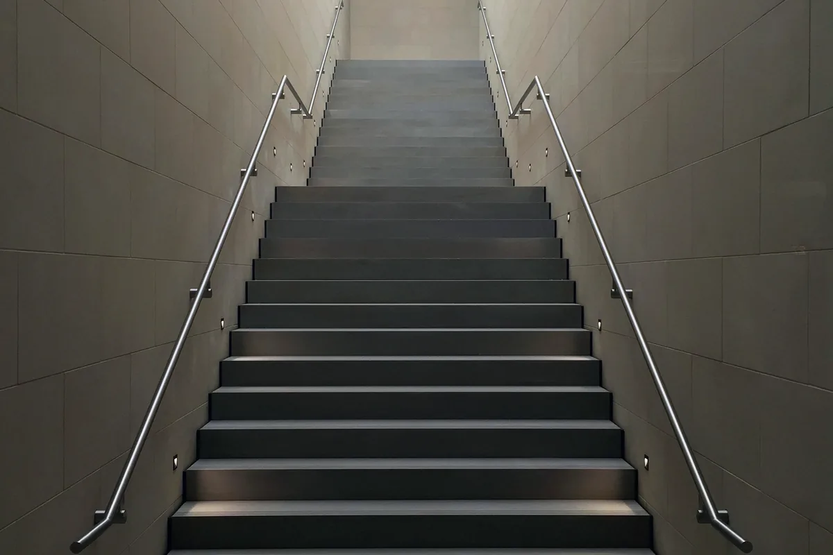 Un escalier en pierre claire qui monte entre deux murs, éclairé par le soleil du matin